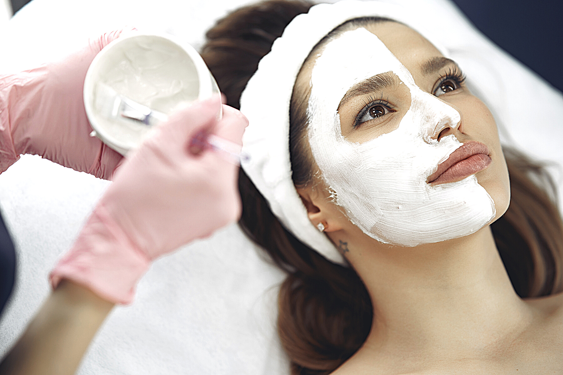 Crop unrecognizable beautician applying clay mask to clients face